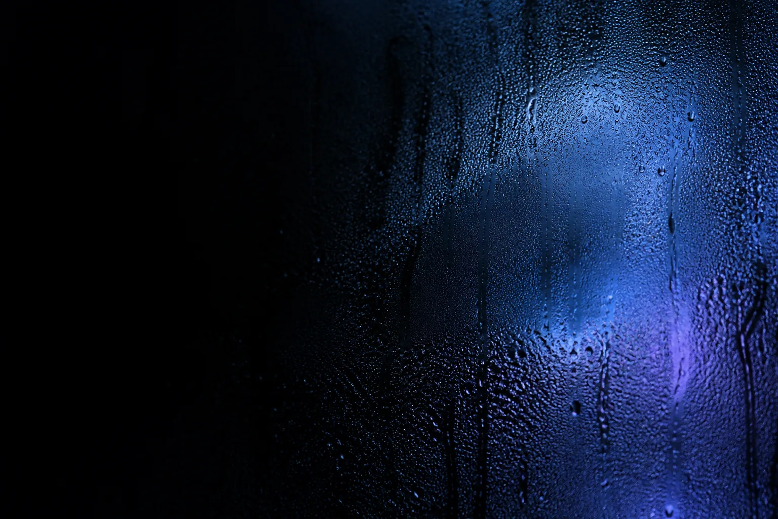 Breath condenses on dark glass around a hidden blue light.
