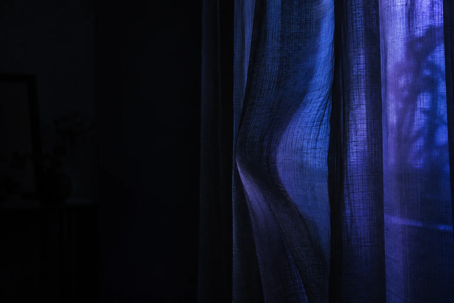 A translucent curtain lifts with a slow breath in a dark room.